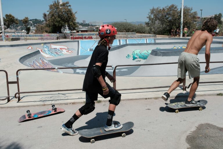 Person skater med et komplet beskyttelsessæt. Personen har hjelm, albuebeskyttere, håndledsbeskyttere og ankelbeskyttere på. I baggrunden ses skaterparken med dens ramper og graffiti.