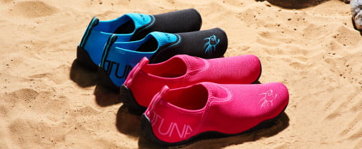 8dsd asd9u8 a9 dhtu89 To par badesko, et par i blå og et par i lyserød, er sat på stranden.