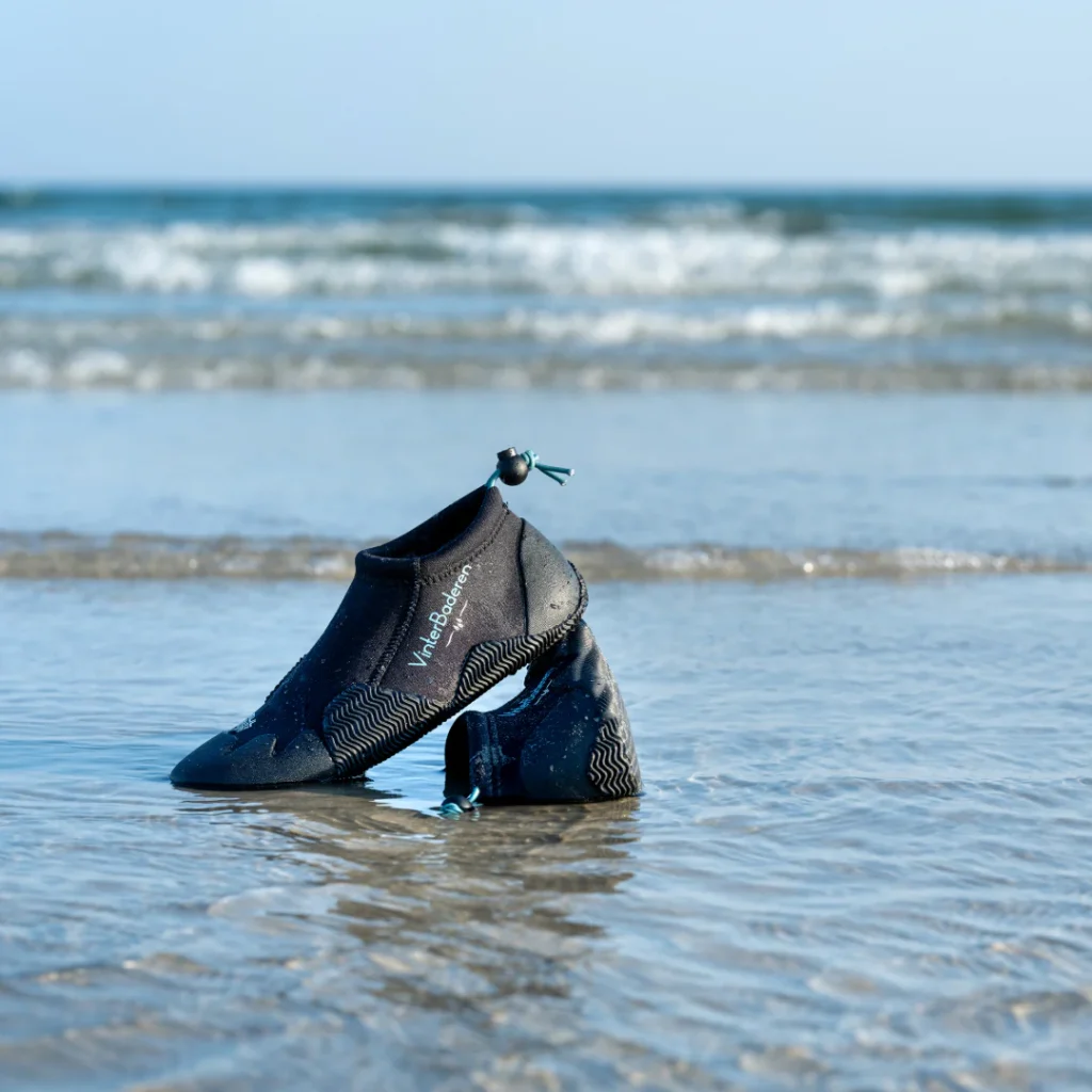 h8odcs 9a8sd n8dasp Badesko er sat til opvisning i vandet med bølger i baggrunden