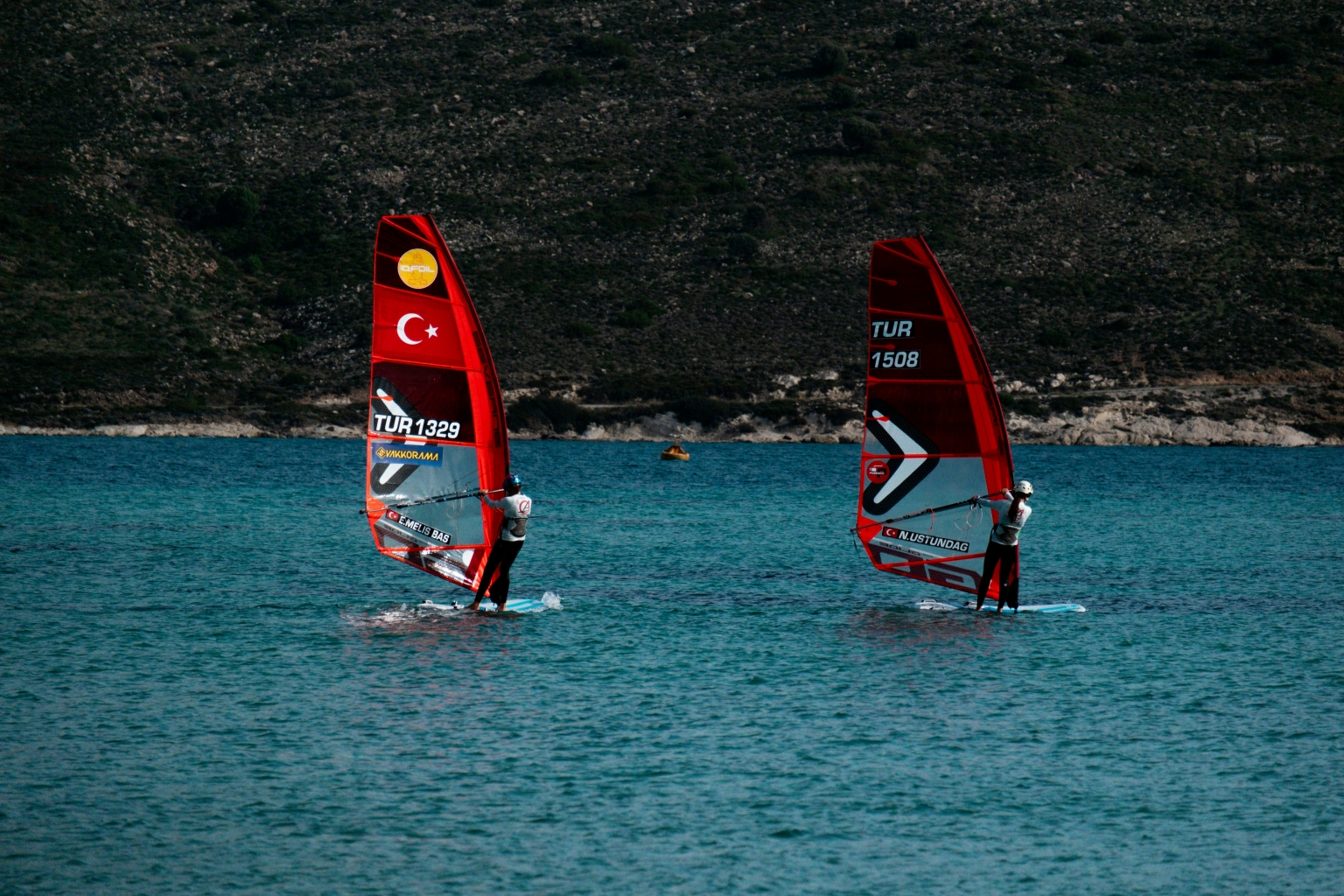 hakan cinar H1f8upzq5WM unsplash To personer er ude og Windsurfe i det gode vejr. Vandet er lyseblåt og kysten bliver lyst op af solen.
