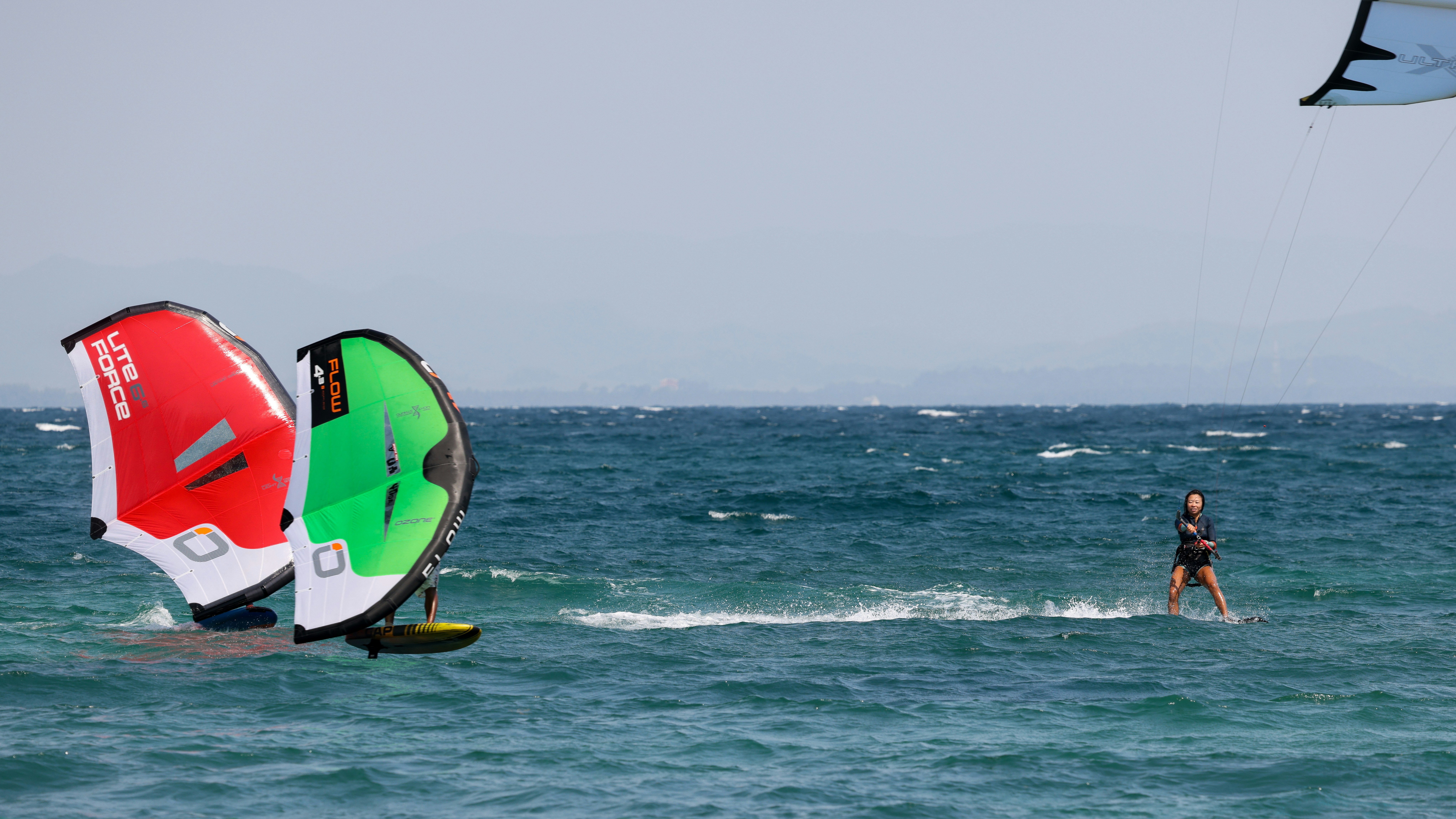 jim thirion ac90zbjl dI unsplash To personer er ude og lave ræs med deres nye Wingfoil. Den ene er i rød, og ligger bag den anden grønne som fører