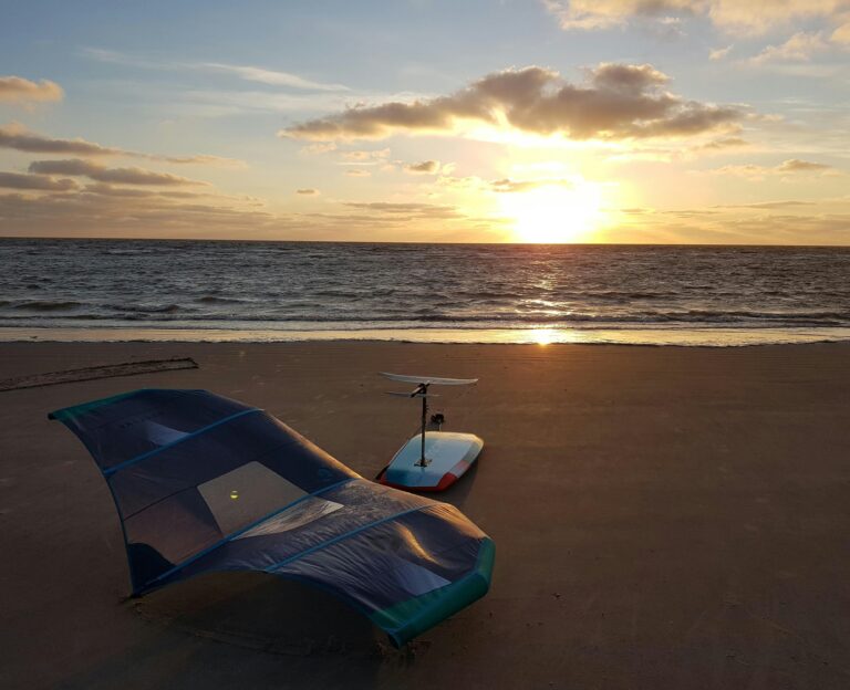 wing foil 1tnVa5dS M4 unsplash Wingfoil board og udstyr ligger på stranden med en flot solnedgang i vandet