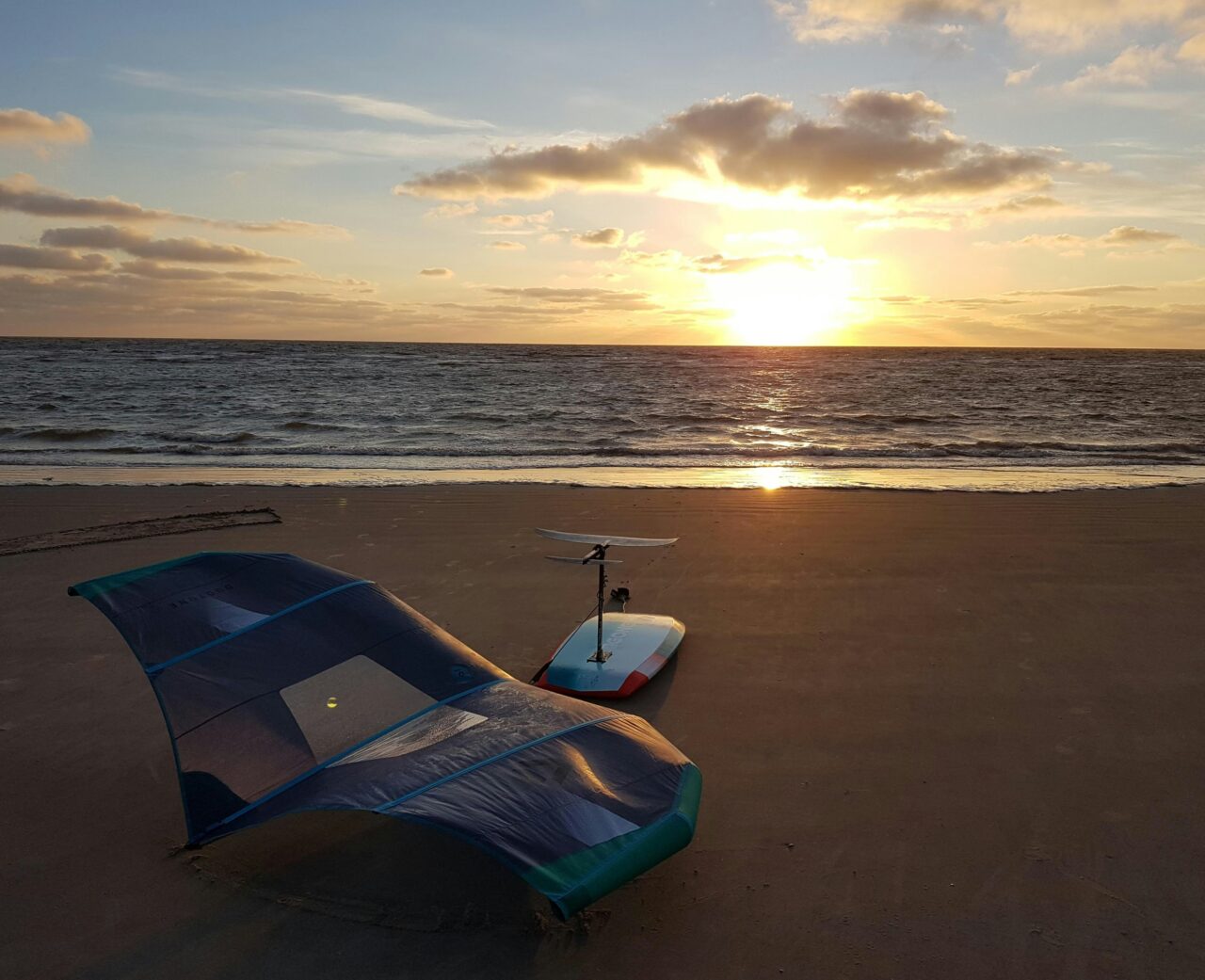 Wingfoil board og udstyr ligger på stranden med en flot solnedgang i vandet Wingfoil board og udstyr ligger på stranden med en flot solnedgang i vandet