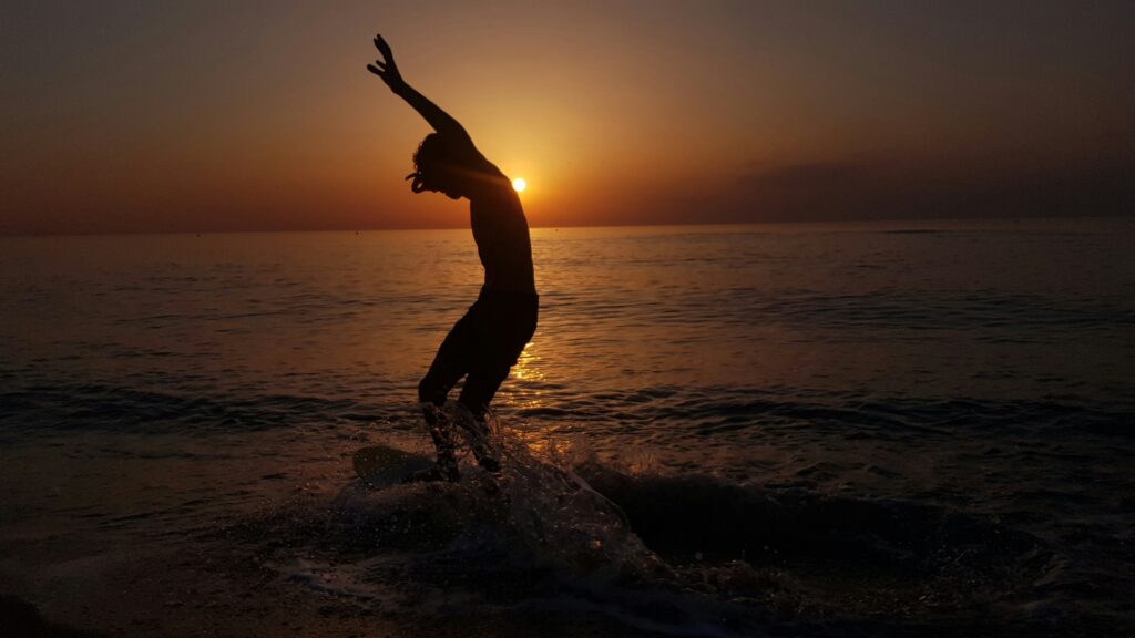 Person står på wakeboard med aftensolen i baggrunden.