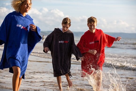Tre personer løber på stranden med badeponchoer på Tre personer løber på stranden med badeponchoer på